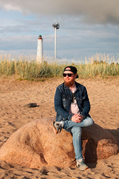 Kuva Matias Hakuntista istumassa rantakivellä. Taustalla näkyy majakka.